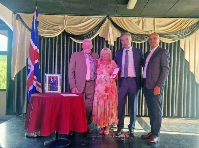 Maria Wilson con su marido y su hijo mientras recibe su BEM de manos del embajador británico Sir Alex Ellis